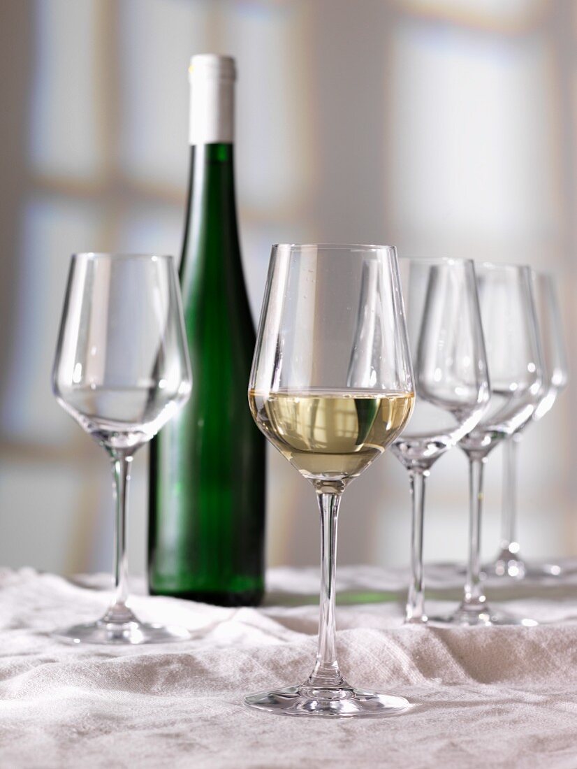 A glass of white wine, a bottle of wine and empty glasses