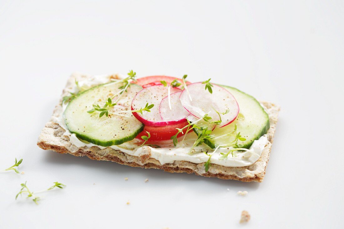 A crispbread topped with cucumber, tomato, radishes and cress