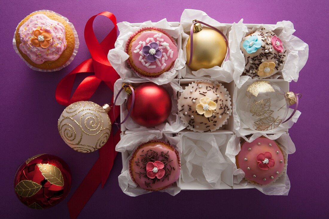 Weihnachts-Cupcakes und Petit Fours zwischen Weihnachtskugeln