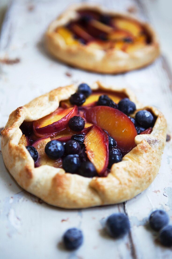 Two blueberry and nectarine galettes on a rustic wooden surface