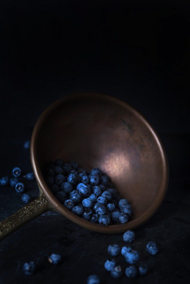 Blueberries in a pewter ladle on a black granite surface