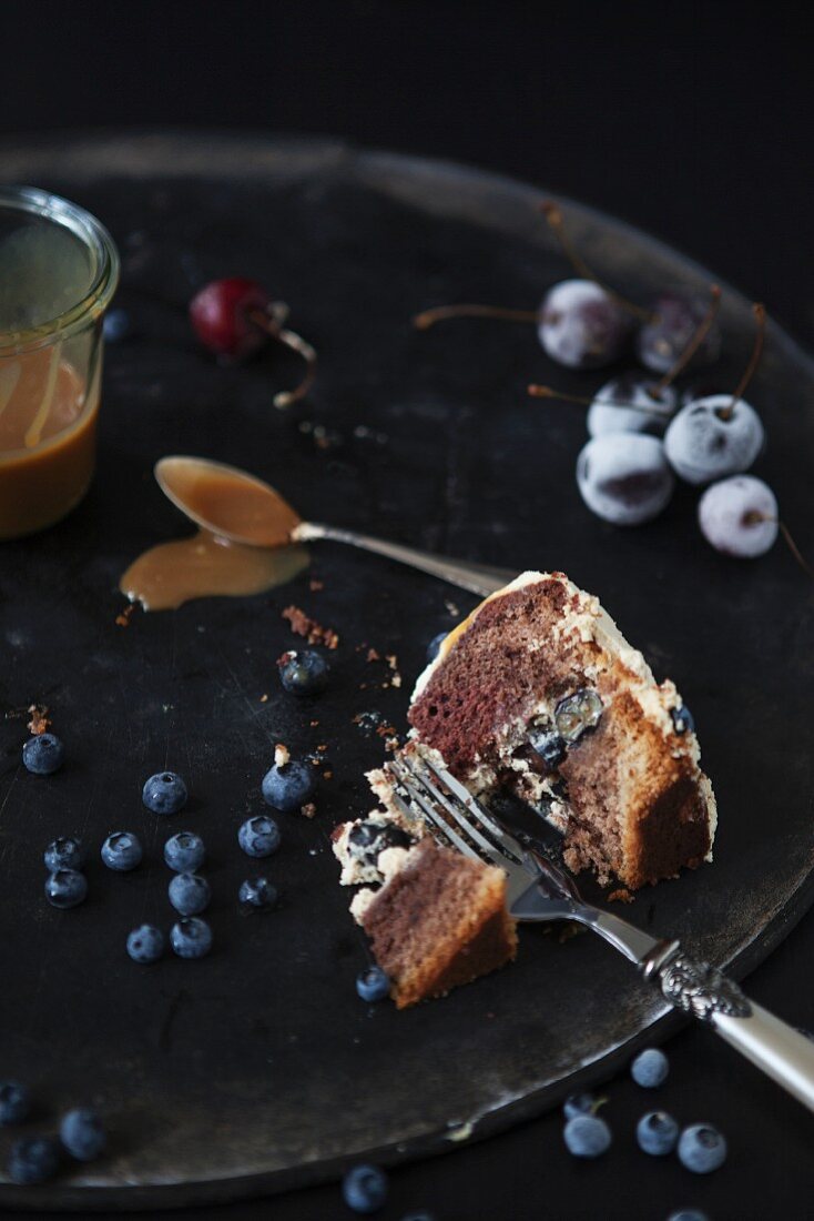 Kuchenstück auf Teller mit Gabel, Blaubeeren, Kirschen und Karamellsauce