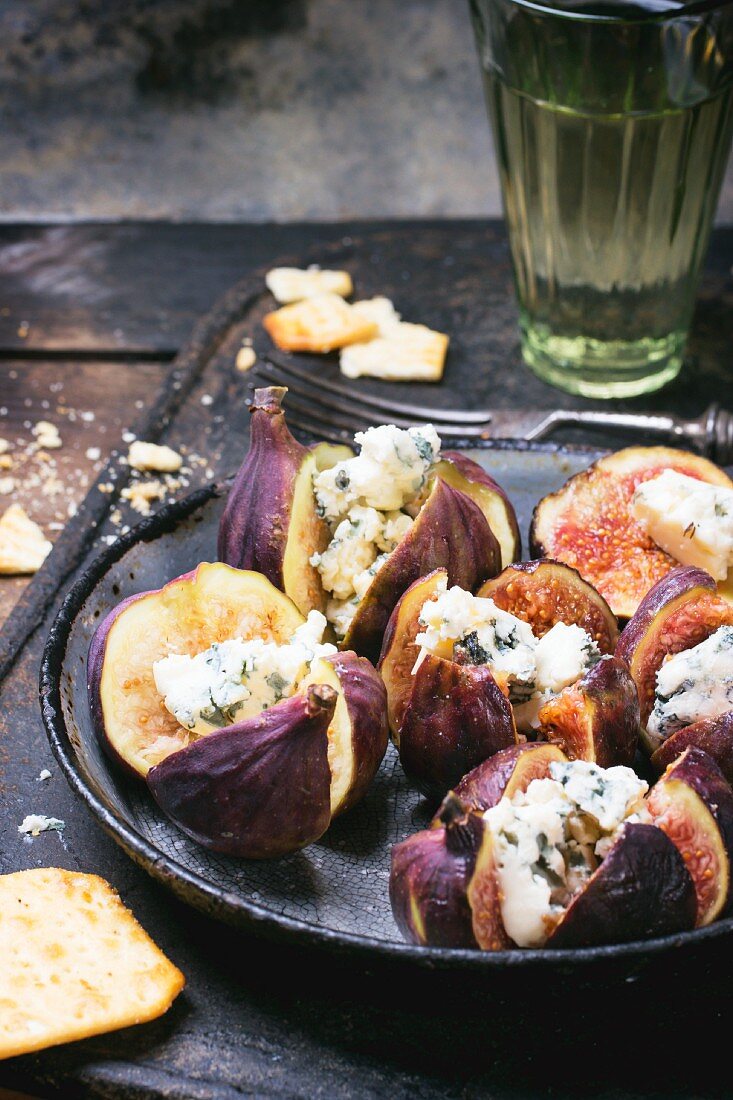 Figs stuffed with blue cheese in an old pan served with crackers and a glass of white wine
