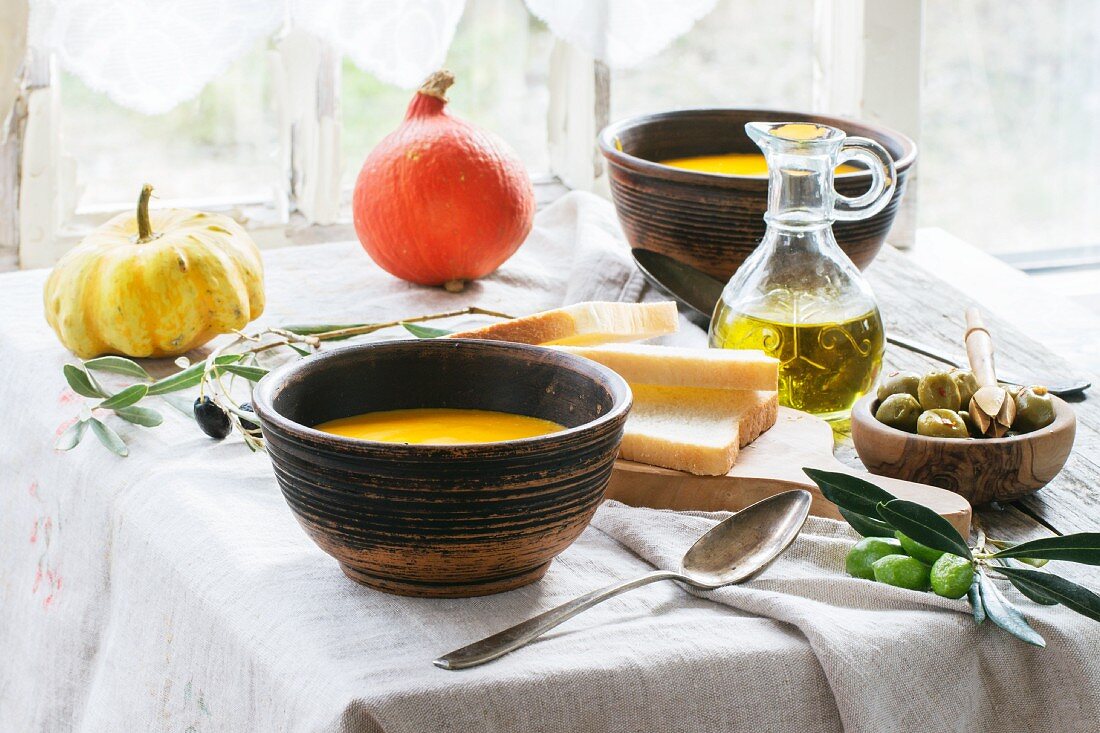 Lunch mit Kürbissuppe und grünen Oliven, serviert auf altem Holztisch beim Fenster