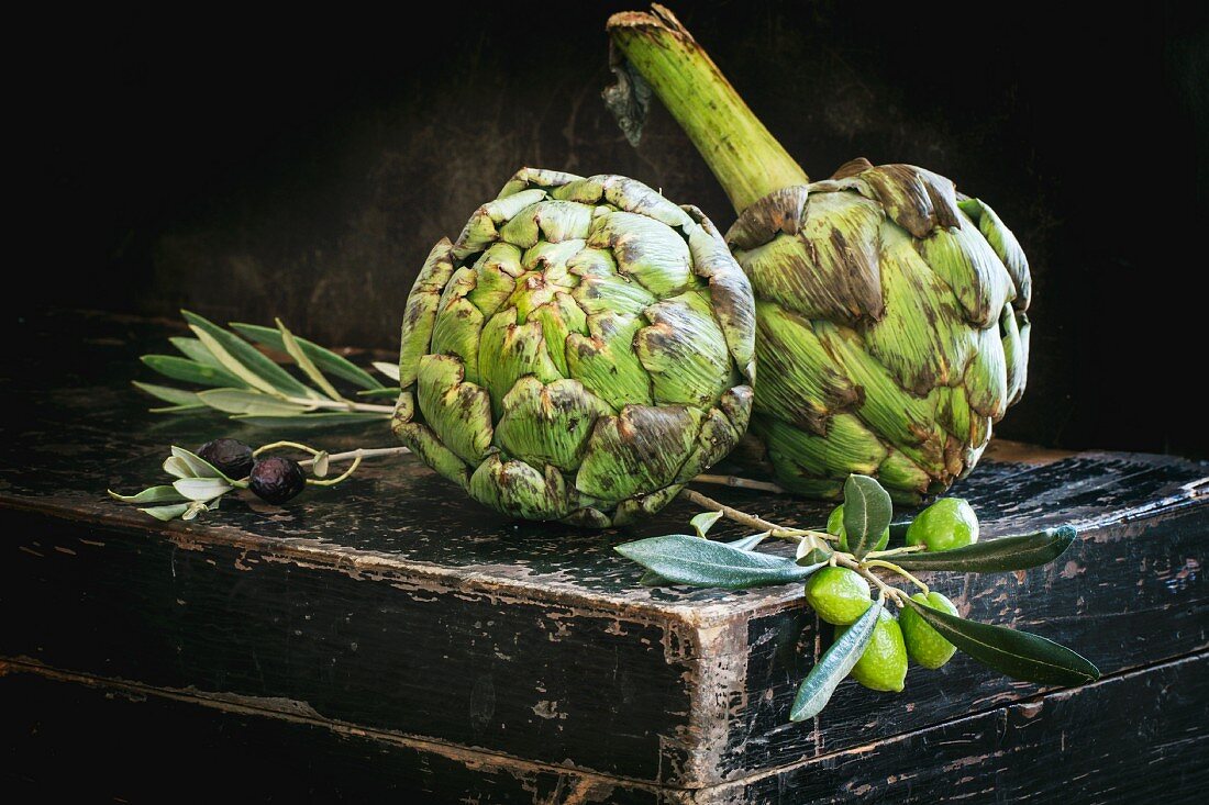 Fresh artichokes and olive sprigs on an old black chest