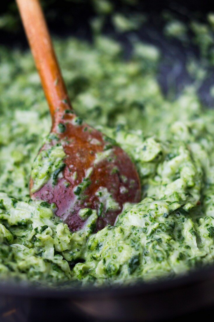 Creamy spinach in a pan with a wooden spoon