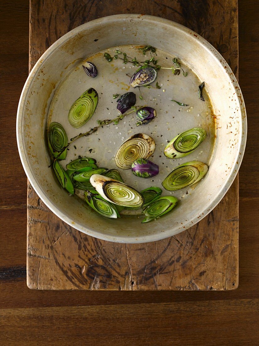 Charred slices of leeks and purple Brussels sprouts with thyme and spices in an old pie dish