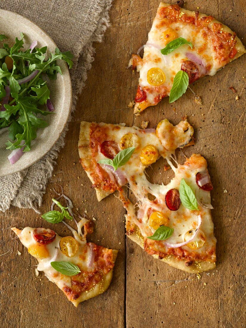 Slices of pizza with red and yellow pear tomatoes, basil and rocket