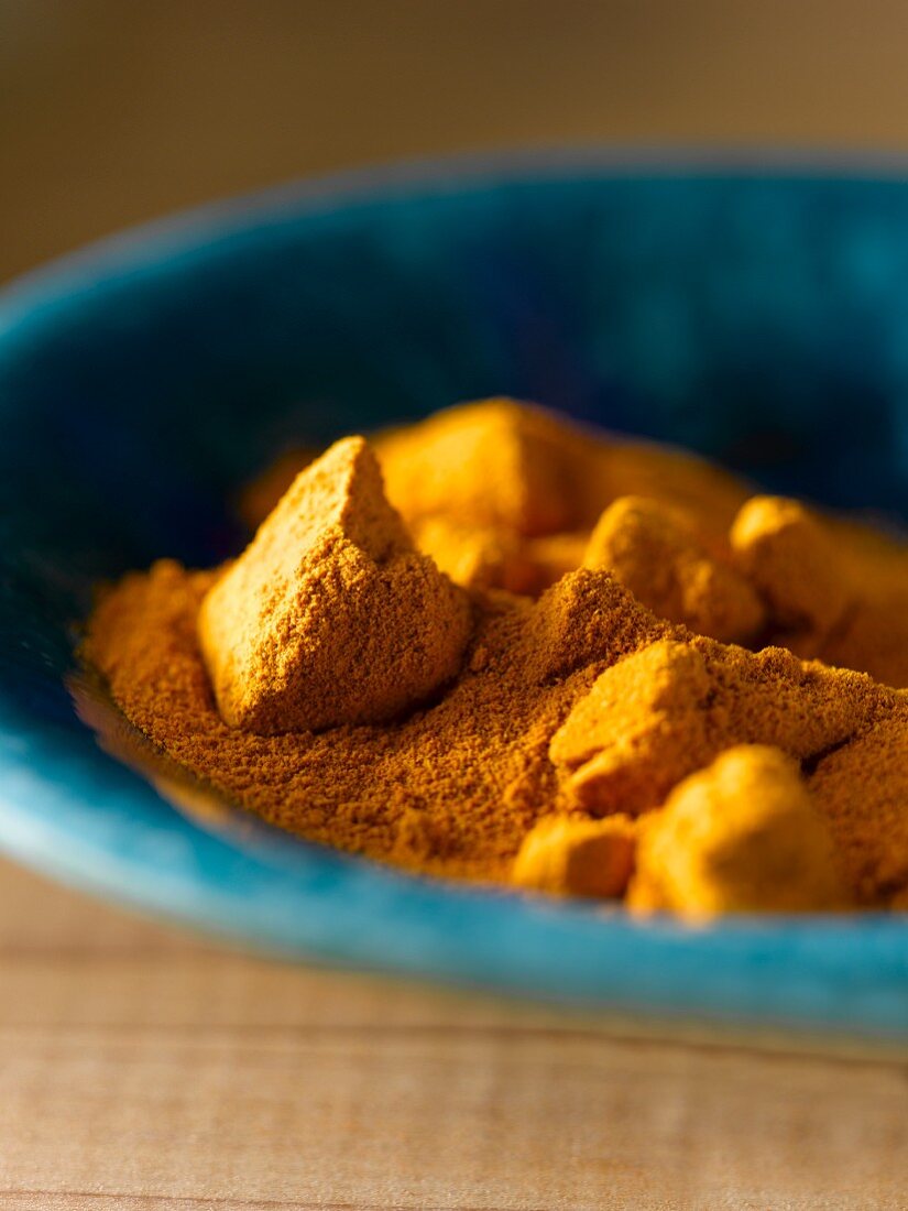 Turmeric powder and chunks in a blue bowl (close-up)