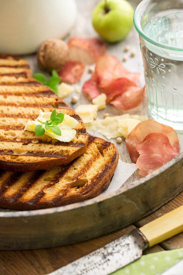 Grilled bread with butter, Parmesan, ham crisps, walnuts, apple and a glass of water
