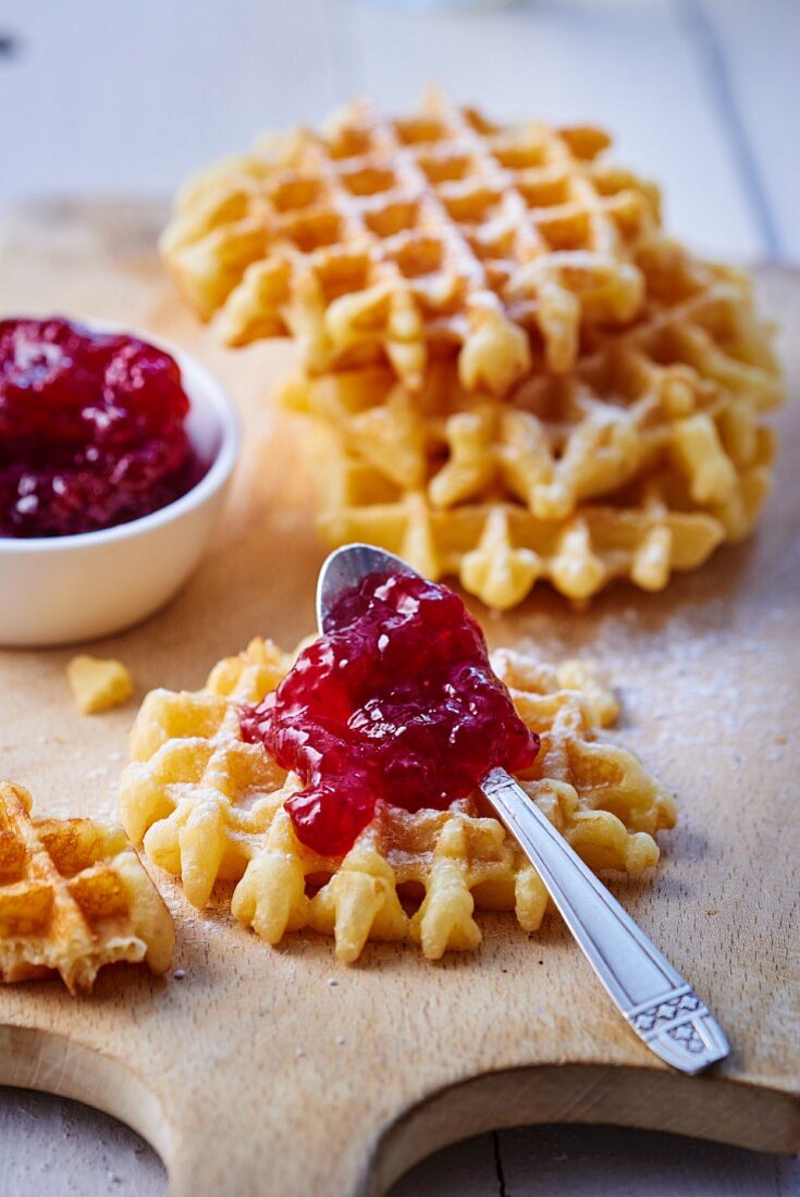 Fresh waffles on a wooden board, one with a teaspoon of strawberry jam