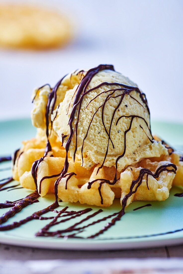 A fresh waffle topped with a scoop of vanilla ice cream and chocolate sauce