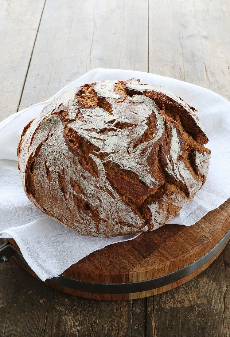 A rustic loaf of country bread on a wooden board with a white cloth