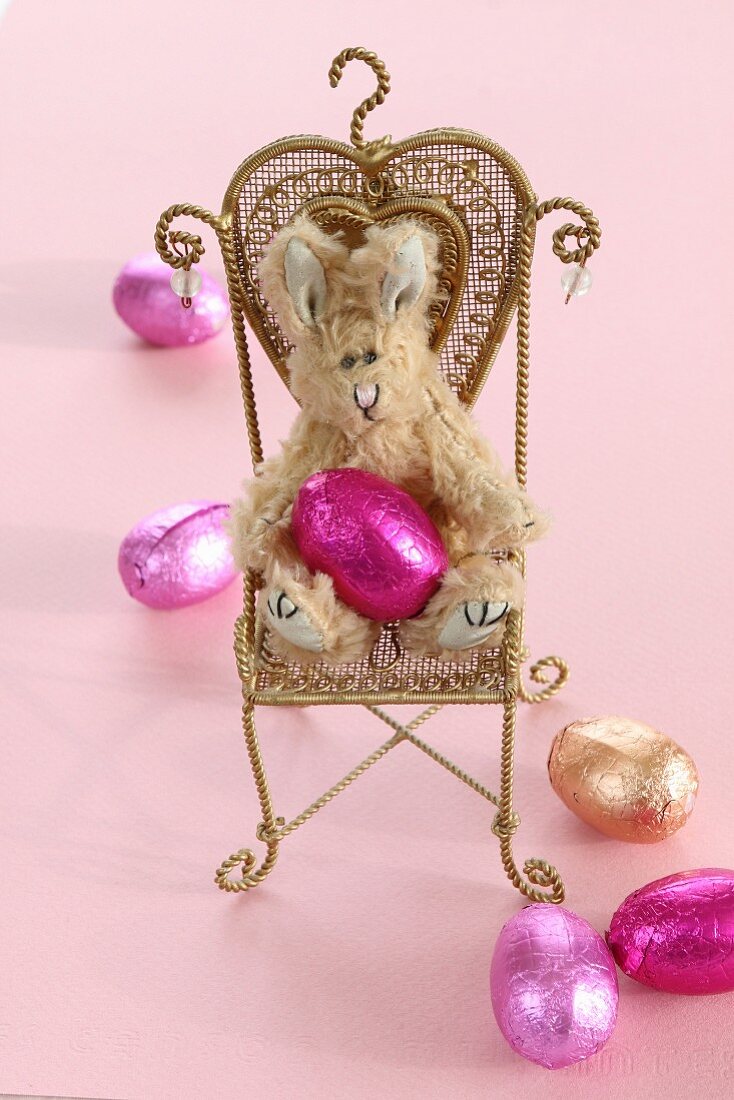 A plush Easter Bunny and chocolate eggs wrapped in foil on a miniature chair