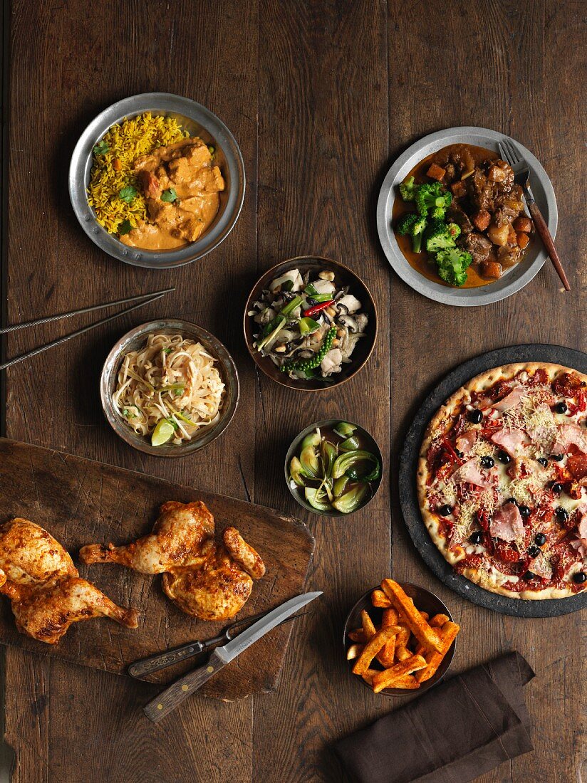 A buffet featuring roast chicken legs, pizza, Irish stew, chicken curry, vegetables, salad, Pad Thai and chips