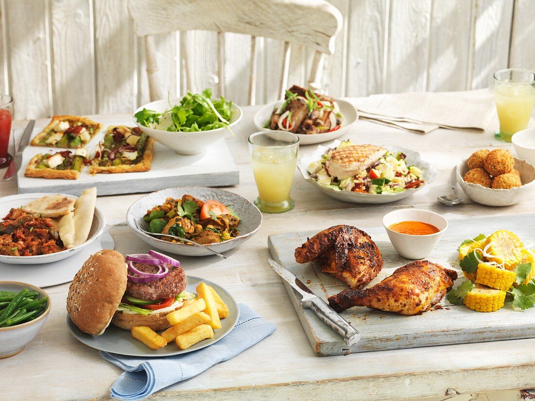 A summer buffet with rocket and rice noodle chicken salad, rice balls, grilled chicken, hamburgers, ratatouille, chicken curry and vegetable tart