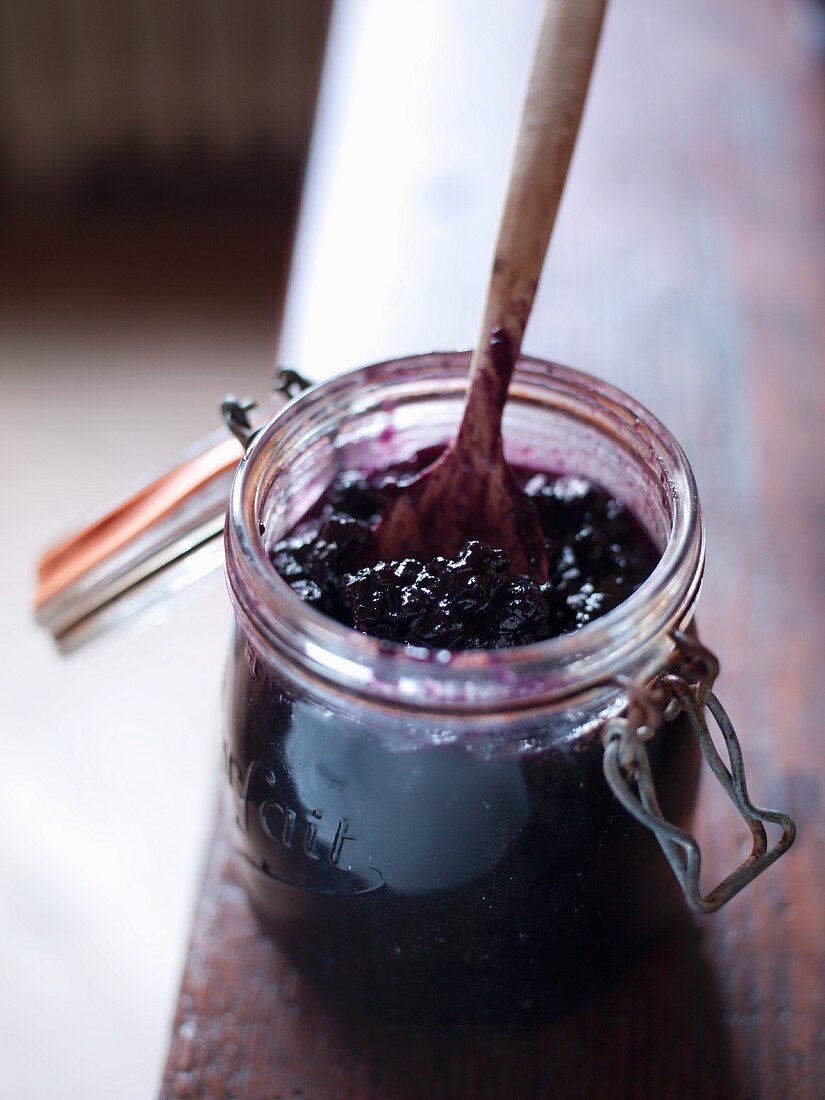 A jar of cassis jam with a wooden spoon