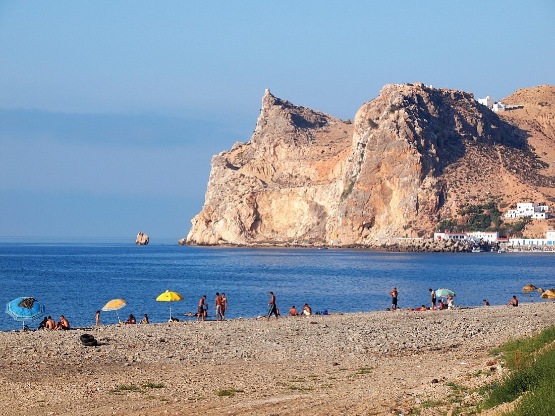 Blick über belebten Strand auf die mächtige Felsenküste bei El Jebha an der Mittelmeerküste Marokkos