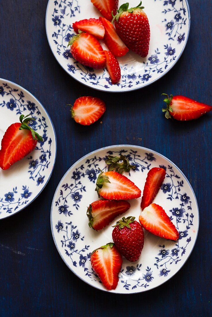 Frische Erdbeeren, ganz und halbiert, auf geblümten Tellern