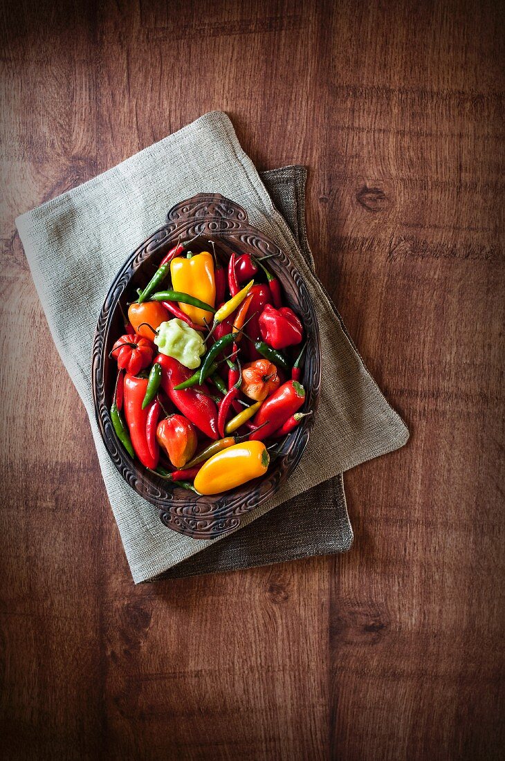 Various fresh chilli peppers in a wooden bowl (seen from above)