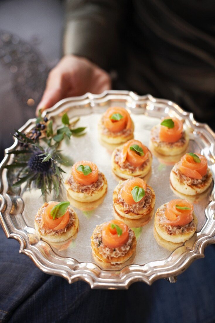 Mini pancakes with smoked salmon and basil on a silver platter