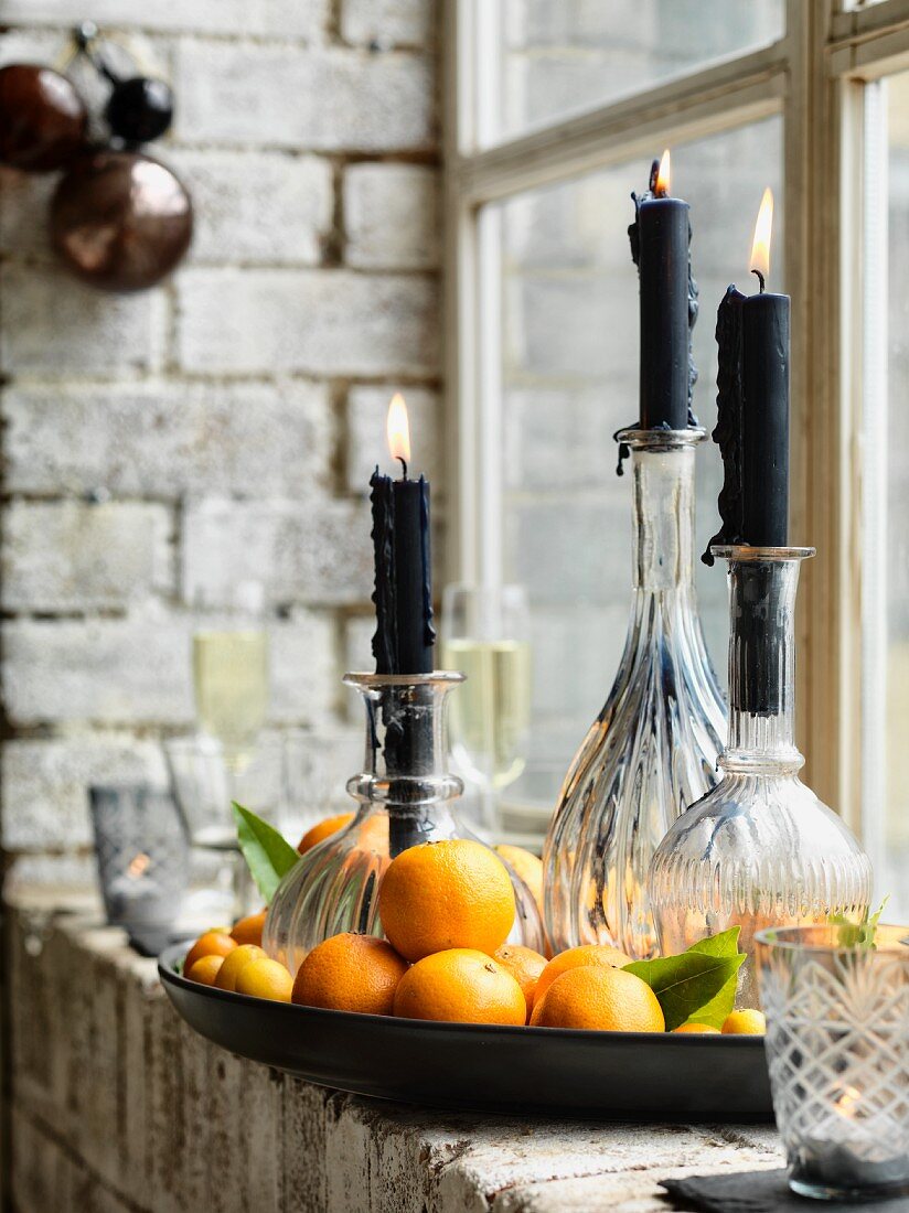 Schwarze Kerzen auf bauchigen Glasflaschen stehen in Schale mit Mandarinen
