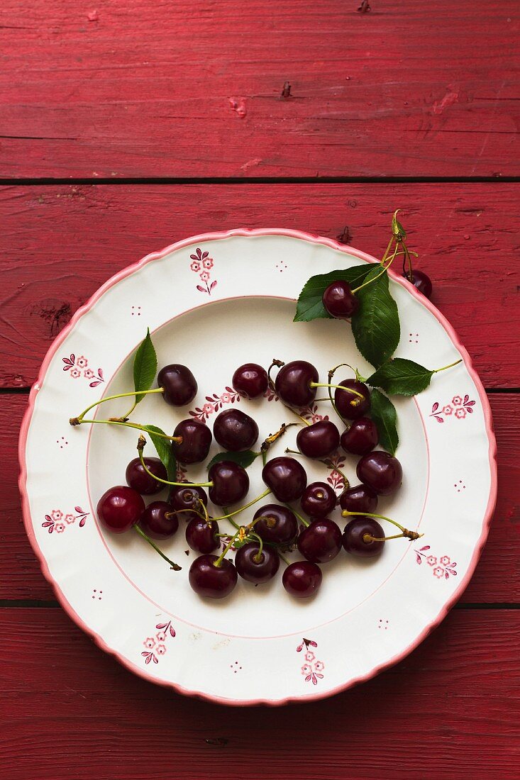 Cherries with leaves on a floral-patterned plates (seen from above)