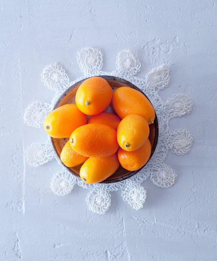 A bowl of kumquats on a lace doily