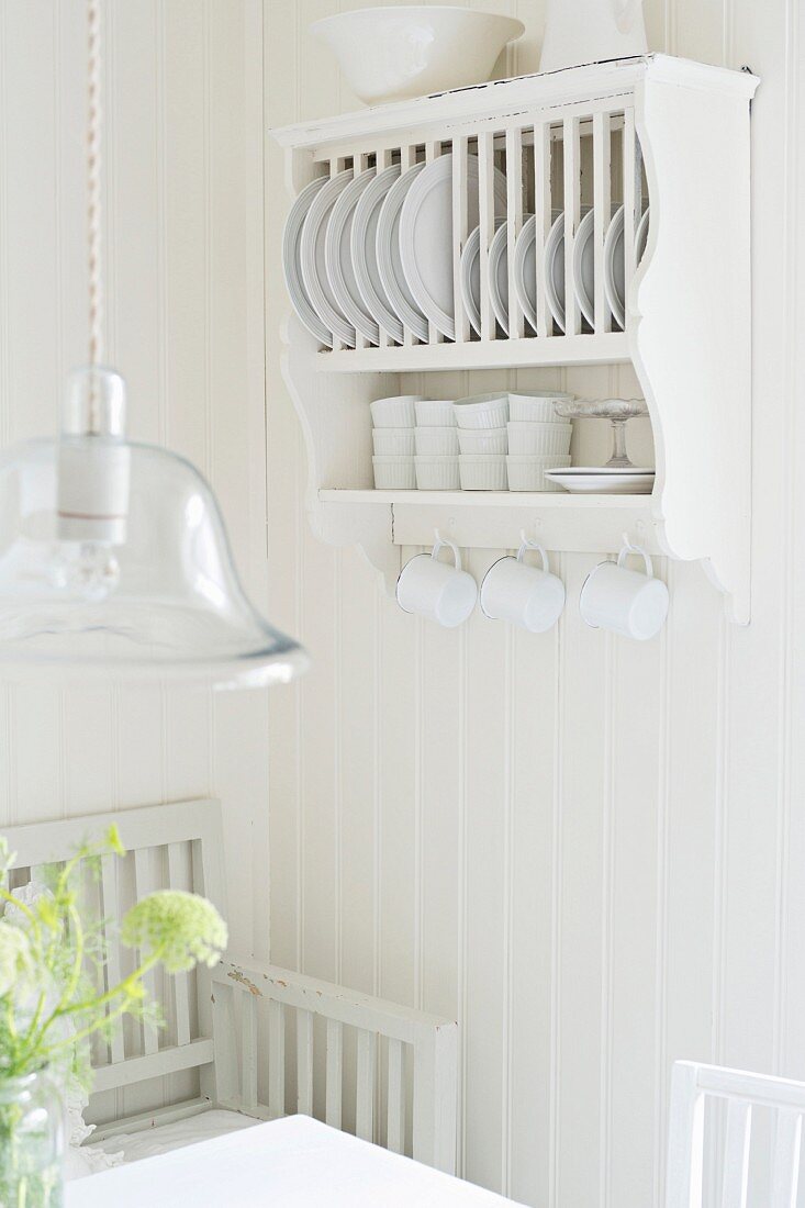 Plate rack with cup hooks and pendant lamp with glass lampshade above dining set in white, Scandinavian kitchen