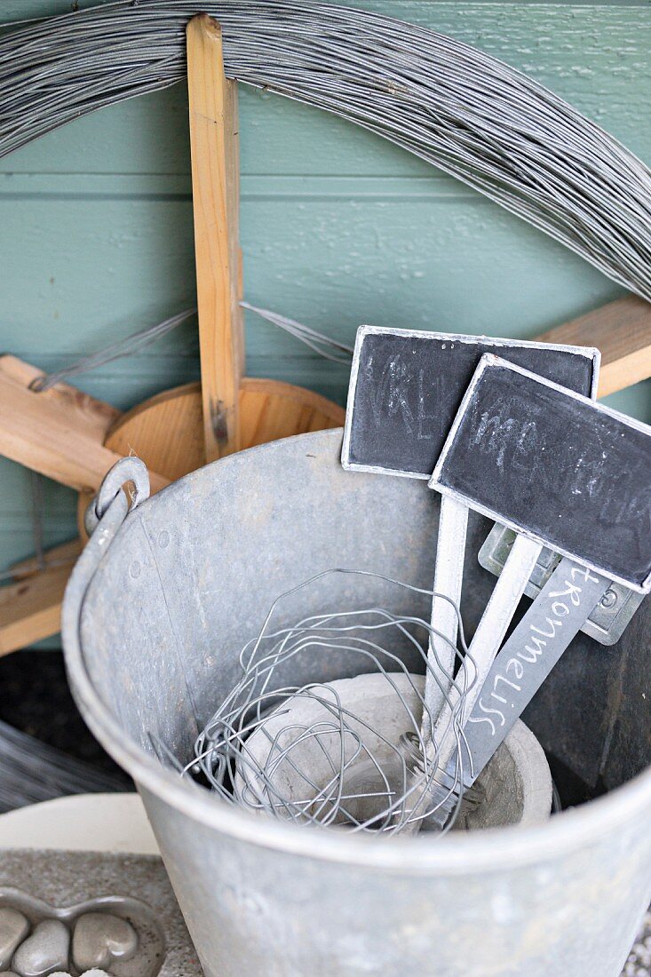 Plant labels in zinc bucket in front of wooden wheel wound in wire