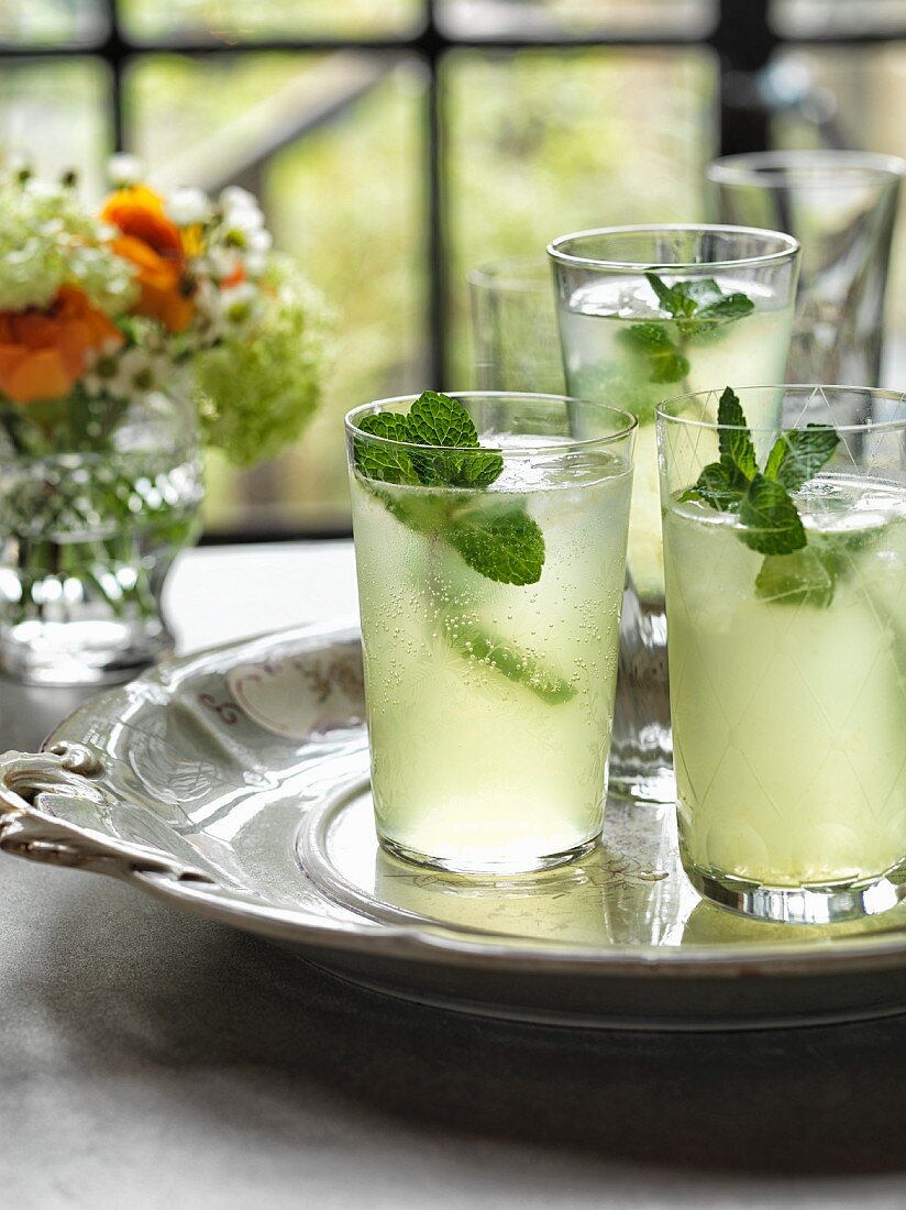 Three glasses of vodka Limoncello garnished with mint on a silver tray