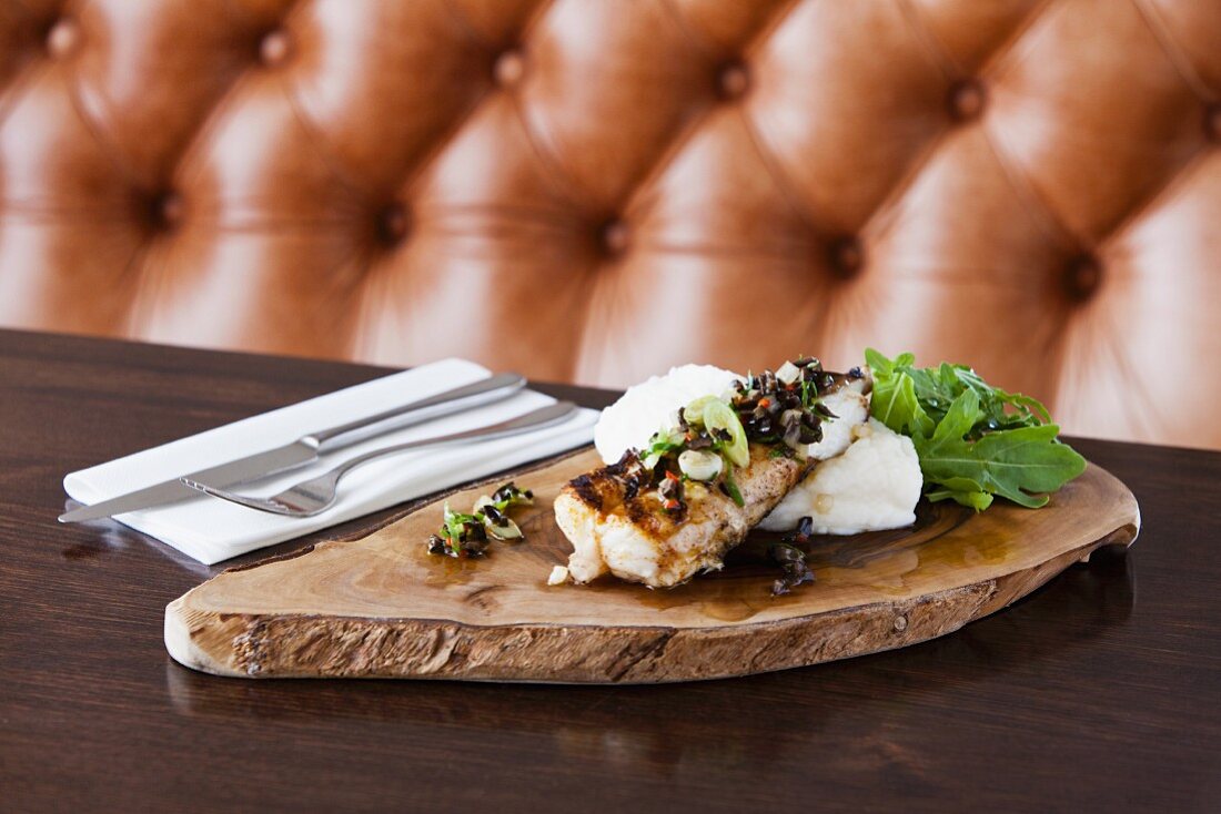 Fisch mit Kartoffelbrei & Rucola auf Holzplatte im Restaurant