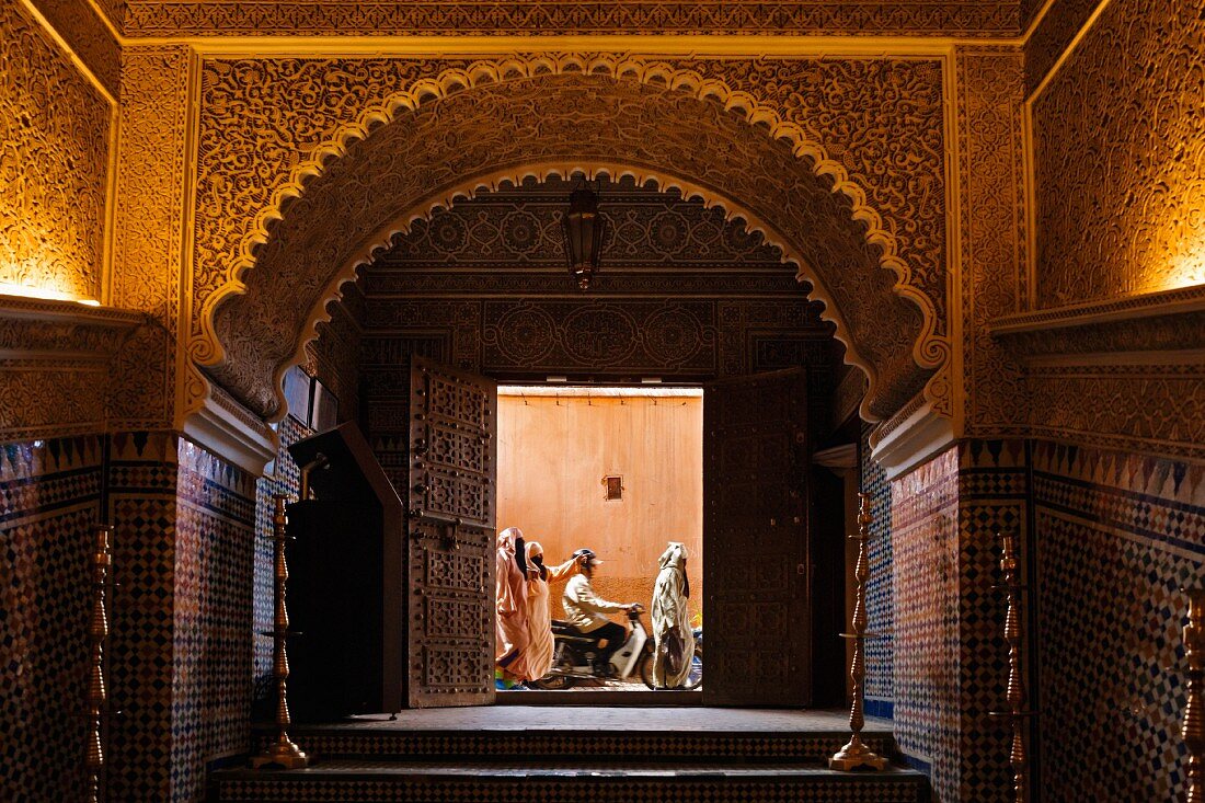 Blick durch prächtiges Portal in eine belebte Gasse Marrakeschs, Marokko