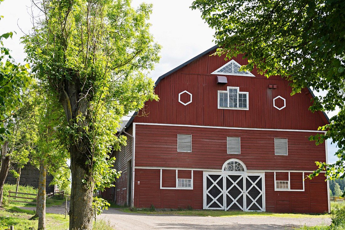 Landhaus mit rotbrauner Holzfassade und weiss gerahmte Fenster, sommerlicher Garten