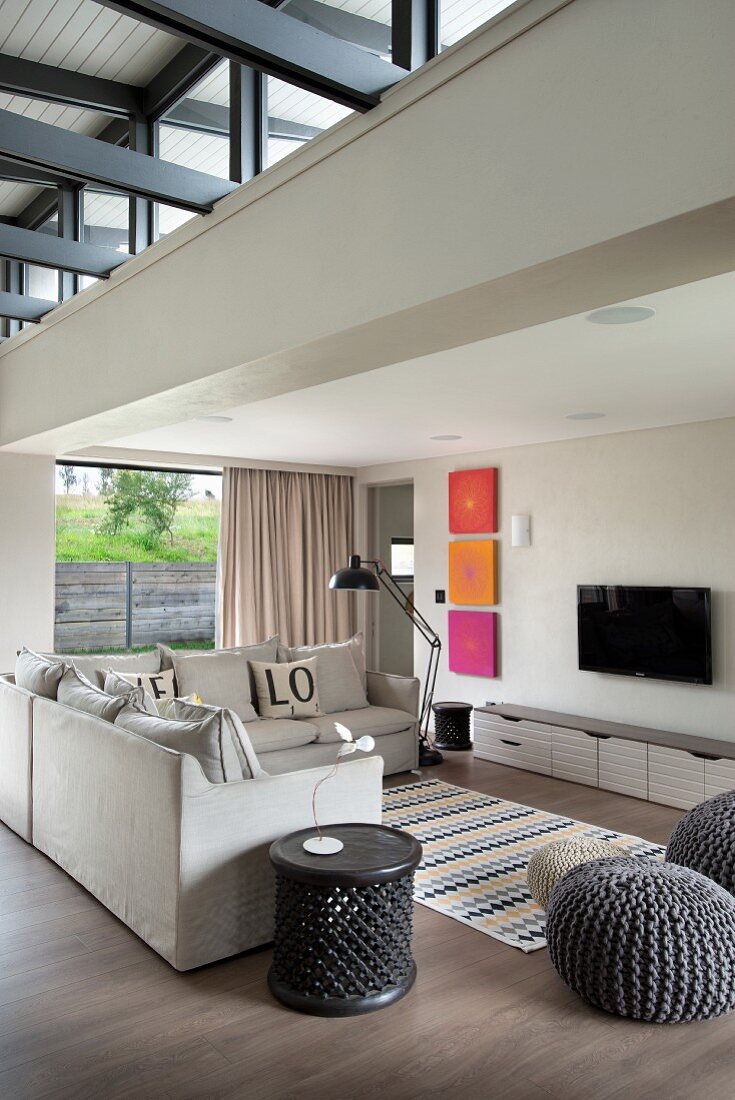 Lounge area with several grey pouffes and pale sofa below mezzanine in open-plan, contemporary interior