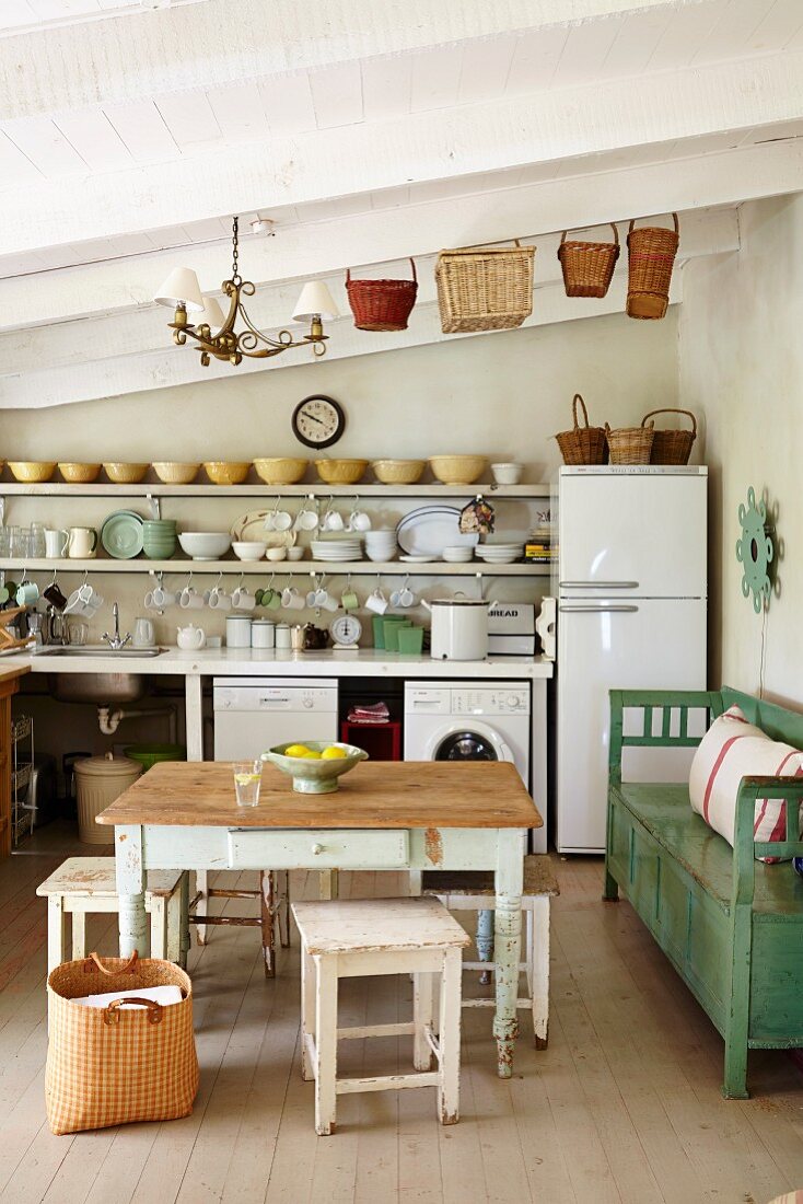 Rustic table and stools and green bench against wall in front of simple kitchen counter in rustic interior