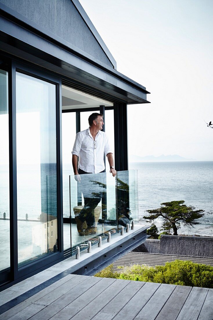 Contemporary house; man leaning on glass balustrade in open balcony doors