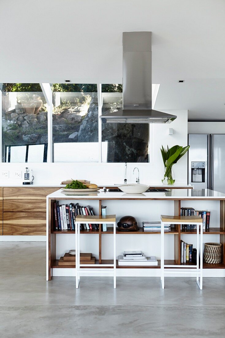 Bar stools at free-standing island counter below extractor hood in open-plan designer kitchen