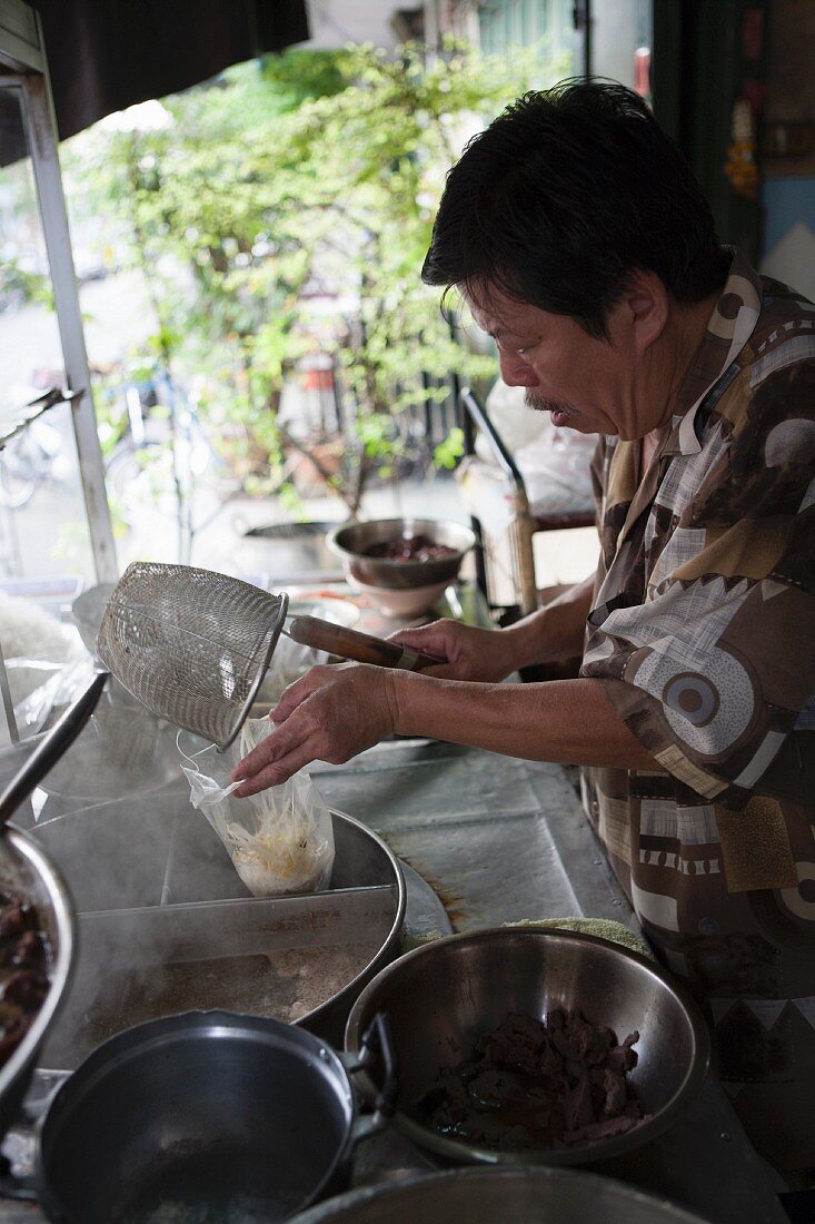 A man cooking noodle soup in a cookshop in Thailand