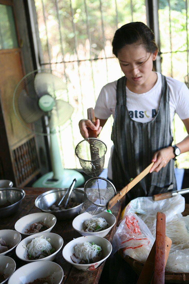 Junge Frau bein anrichten von Nudelsuppe, Thailand