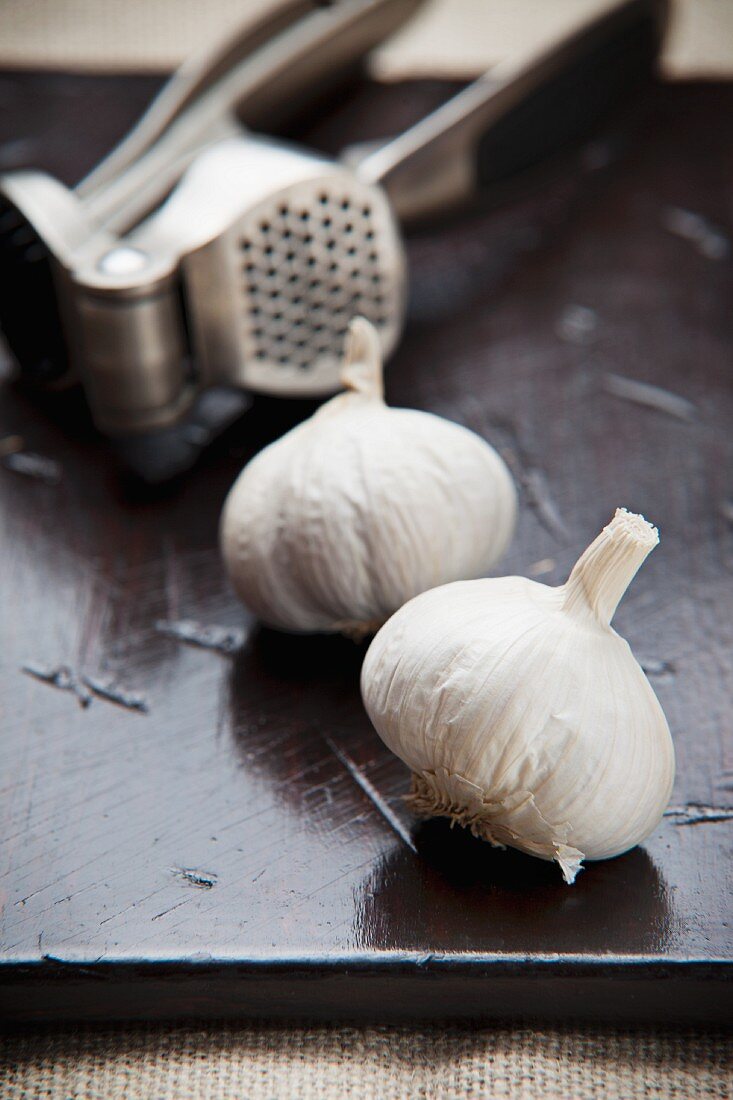 An arrangement of garlic bulbs and a garlic press