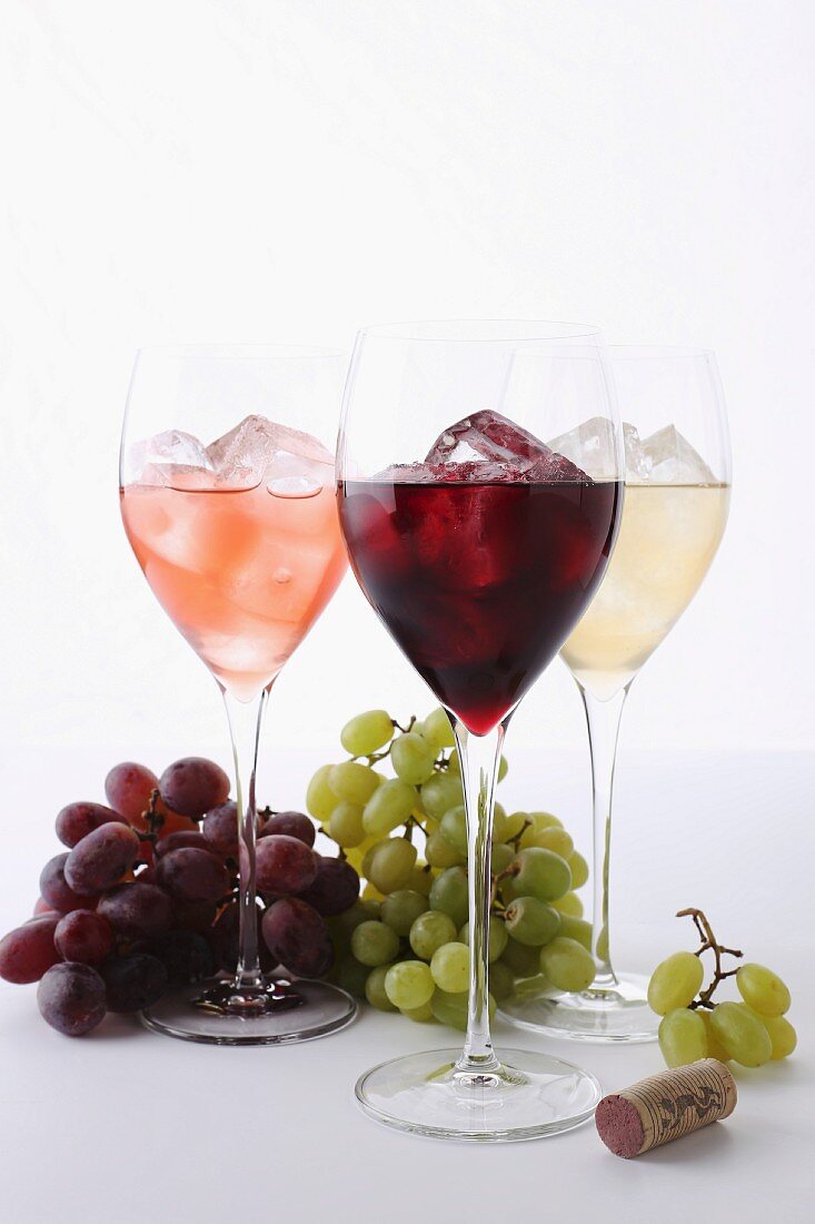 Verschiedene Weingläser mit Eiswürfeln, Trauben und Weinkorken
