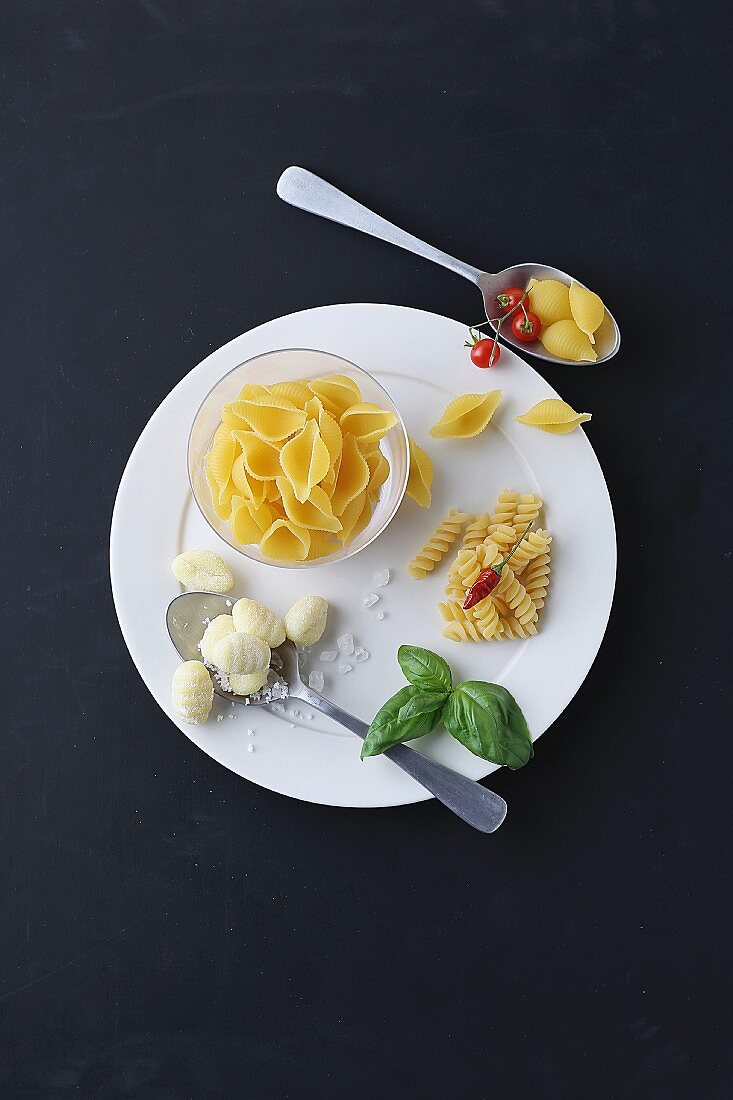 An arrangement of pasta, gnocchi, basil, chilli peppers and cherry tomatoes (seen from above)