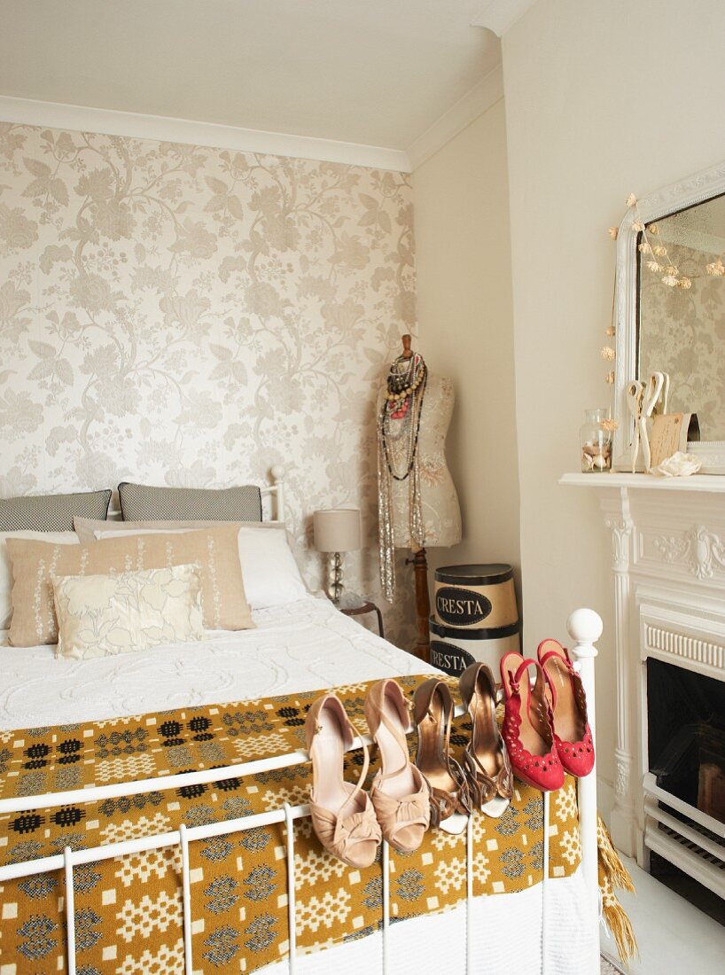 Ladies' shoes hanging on bed frame; tailors' dummy against floral wallpaper in background