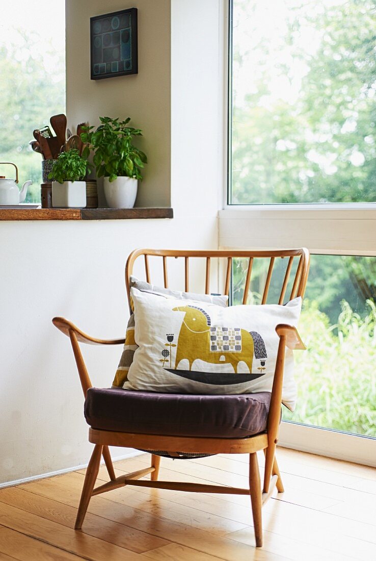 Fifties armchair with cushions next to glass wall and potted herbs on kitchen surface