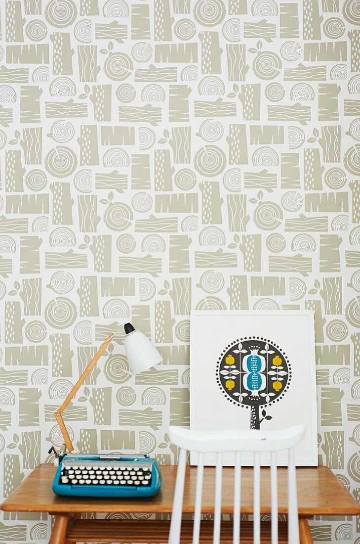 Retro table lamp and typewriter on wooden table against patterned wallpaper