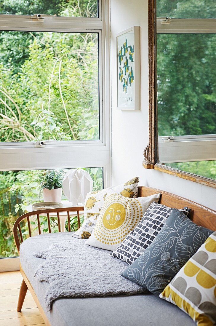 Scatter cushions and grey seat cushions on fifties bench next to glass wall with view into garden