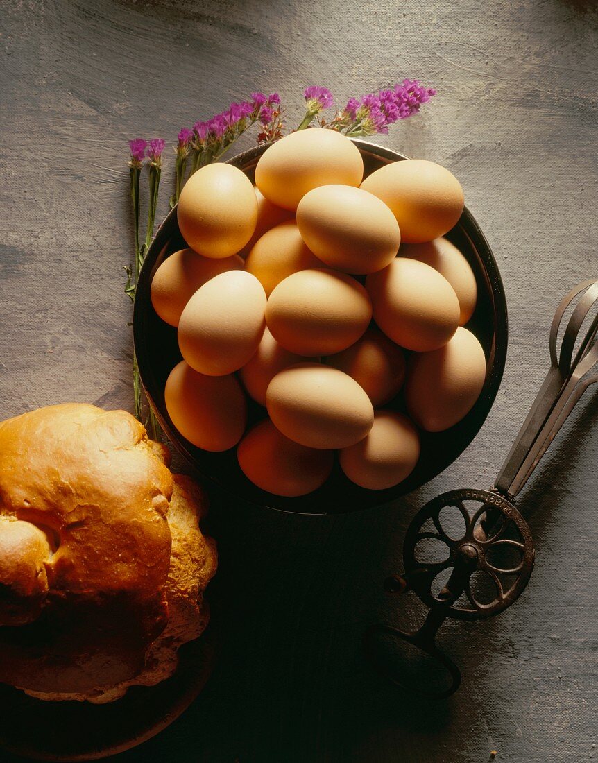 A bowl of brown eggs, an old whisk and bread