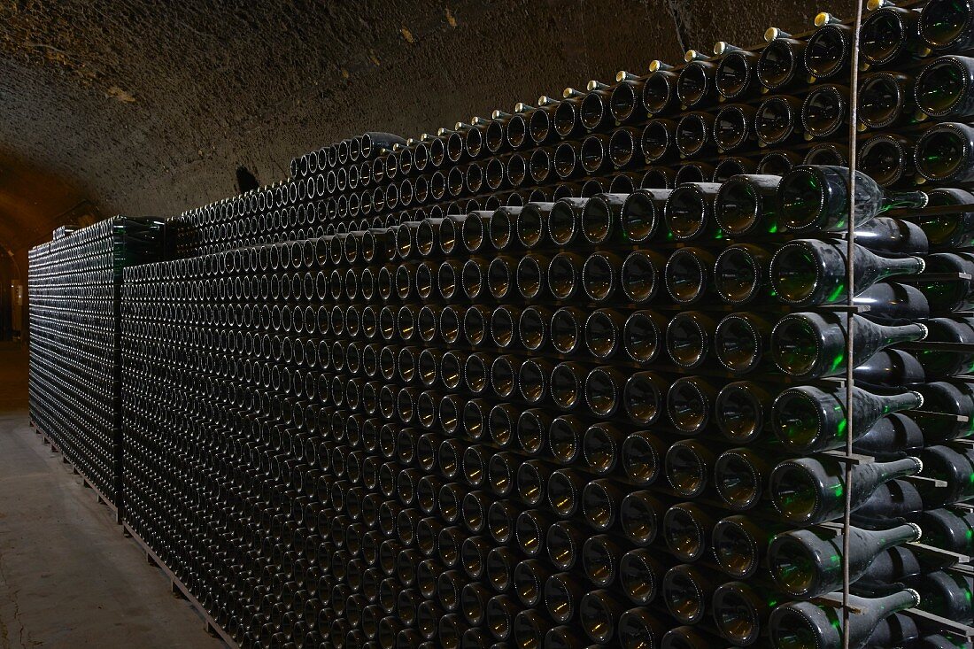 Old wine bottles in metal racks in a vaulted cellar