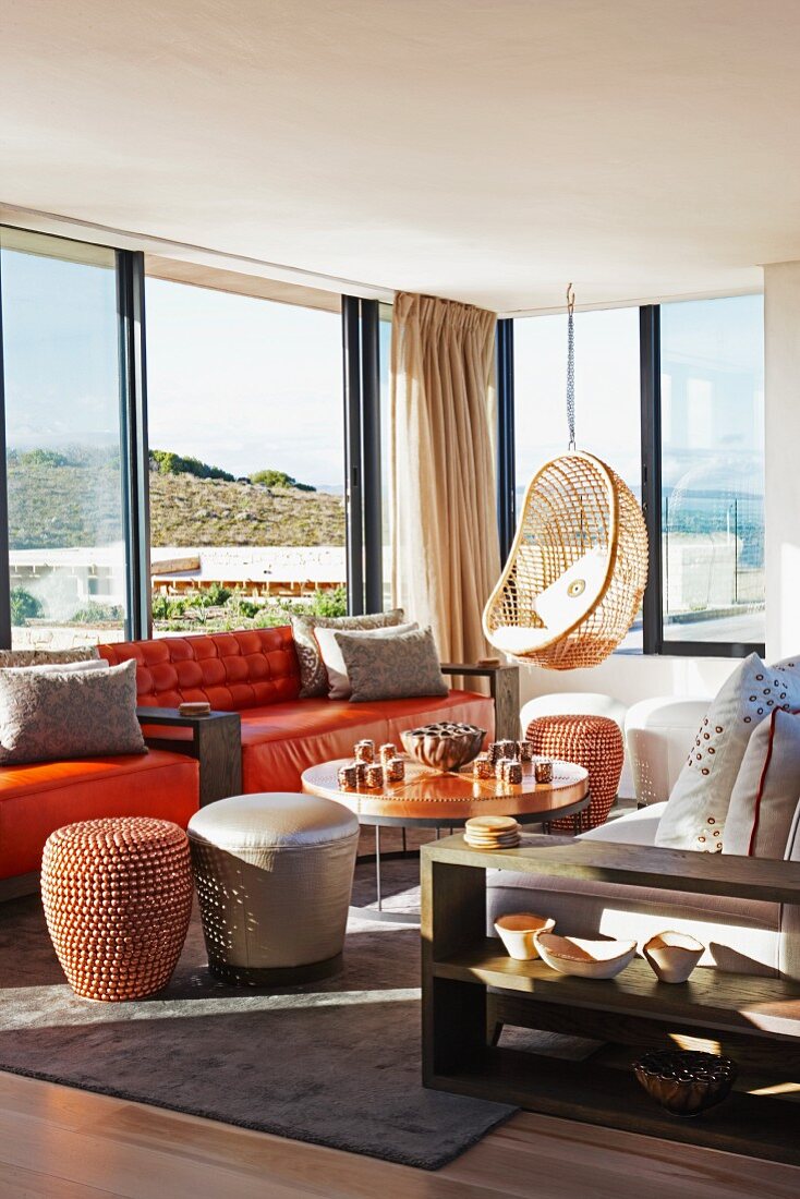 Various seats such as hanging chair, sofa and pouffes in lounge area with view through panoramic windows
